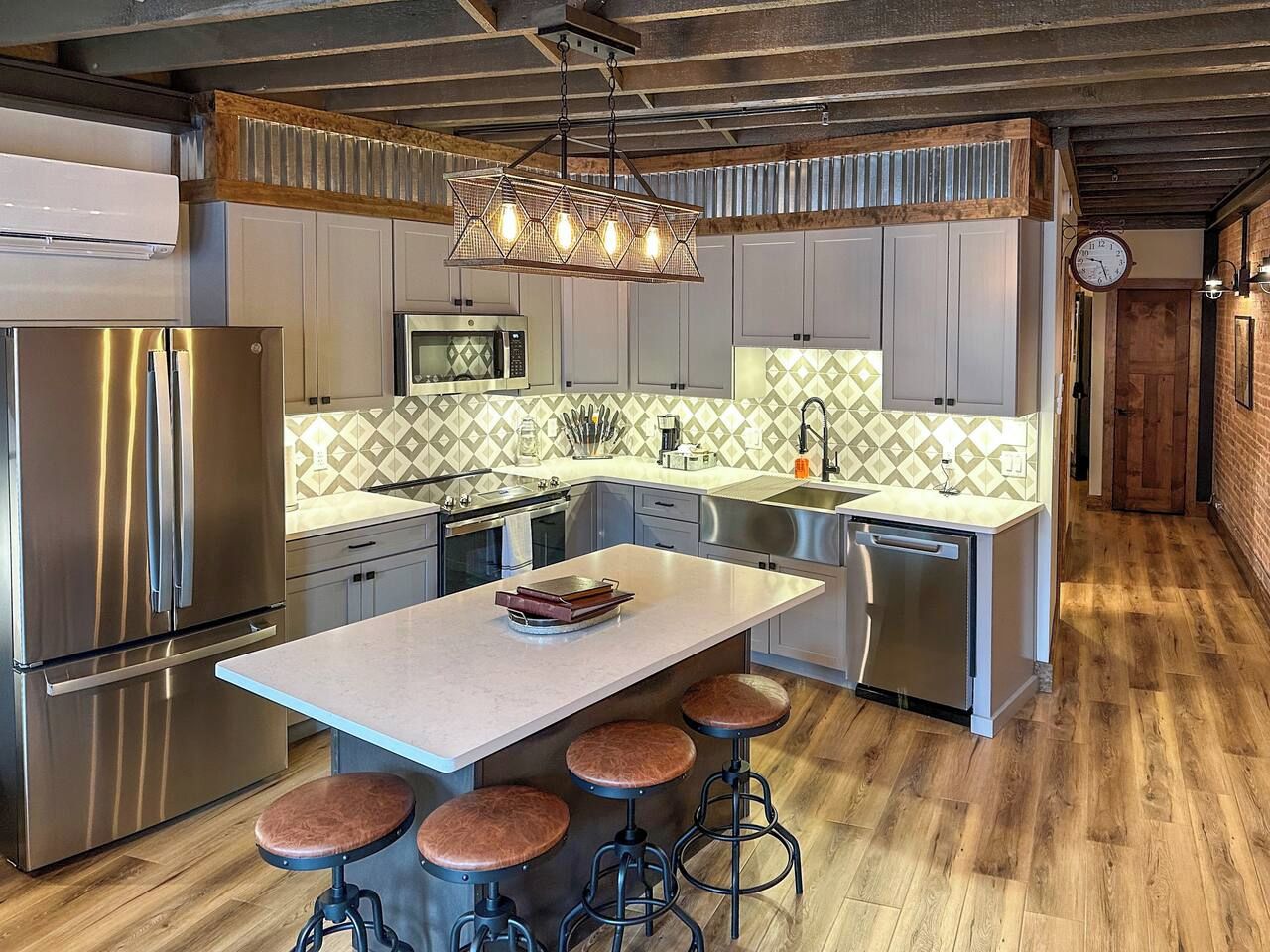A modern kitchen with stainless steel appliances, a central island with stools, and a patterned backsplash.