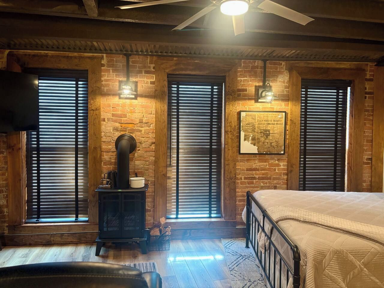 Ein Zimmer mit Backsteinwand, einem Bett, einem Holzkasten und einem Deckenventilator.