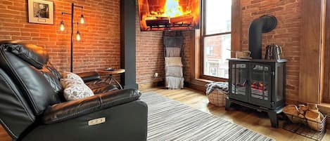 A cozy room with a leather sofa, a fireplace, and a television displaying a fire.