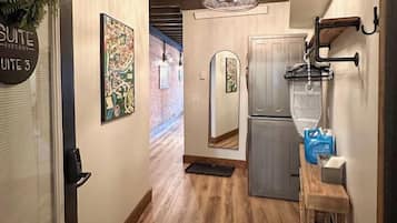 A hallway with a wooden floor, a refrigerator, a sink, and a hanging light fixture.