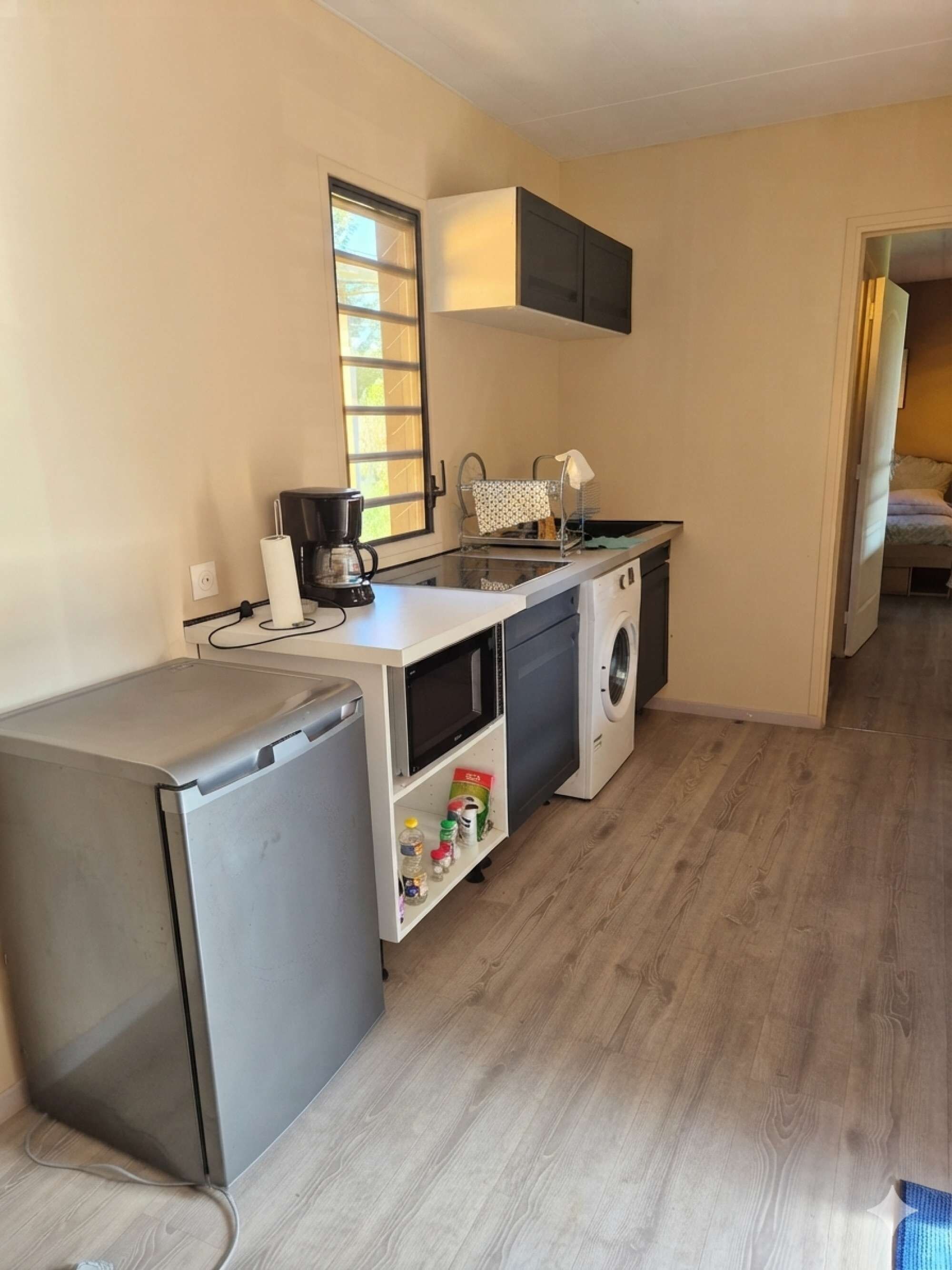 A compact kitchenette with a refrigerator, a coffee maker, a microwave, and a washing machine.