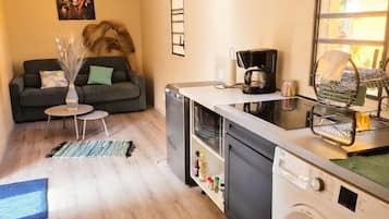 A compact living space with a sofa, a small table, a coffee machine, a washing machine, and a window with a view.