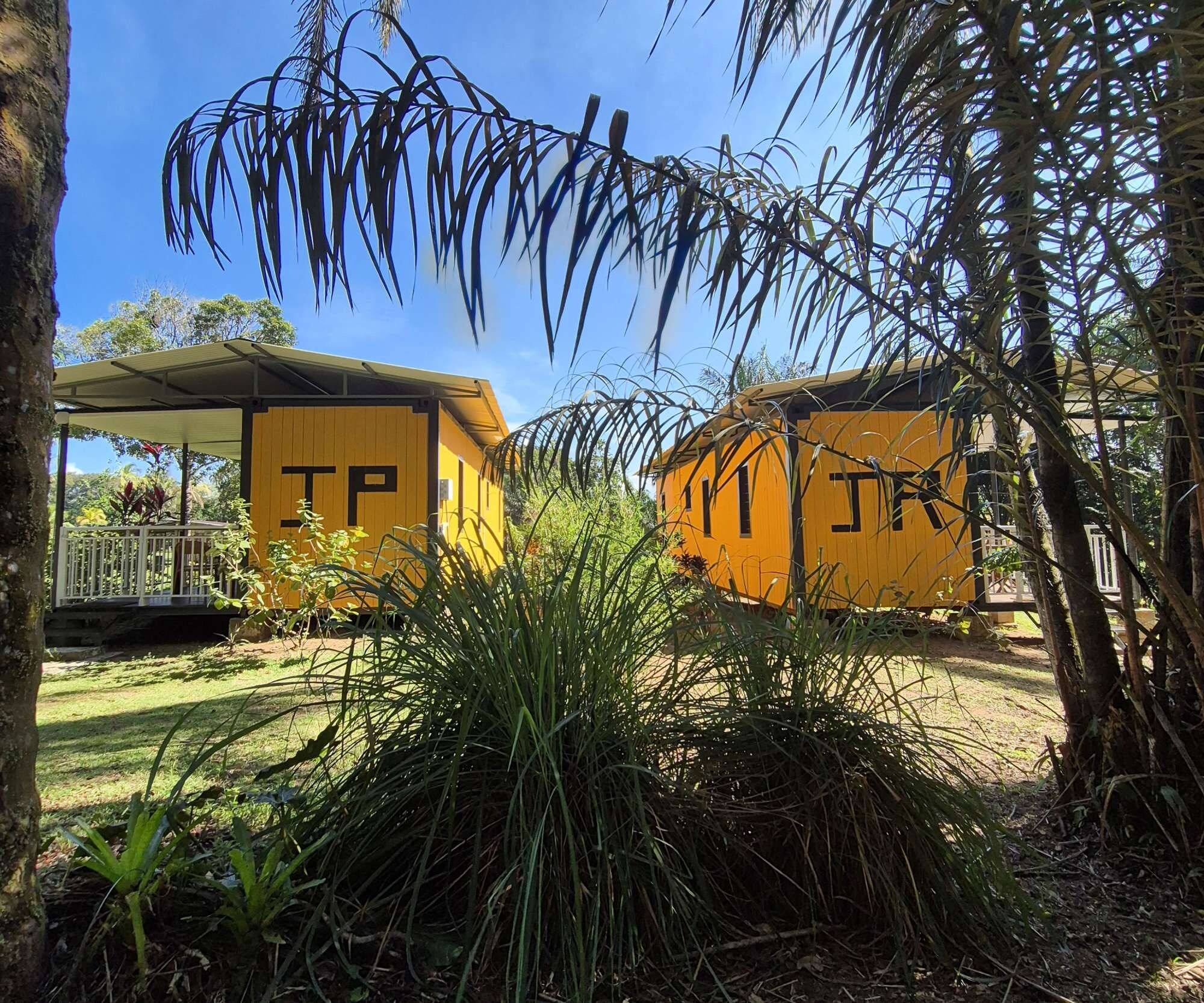 Two yellow cabins with 'TP' on the side, surrounded by greenery and trees.