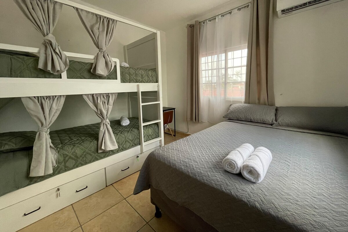 A hotel room with bunk beds, a single bed, a chair, and a window with curtains.