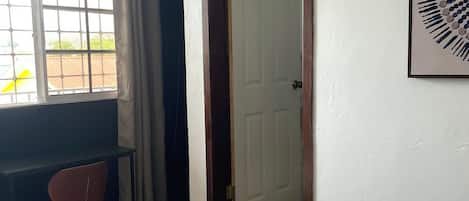 A hotel room with a bed, a desk, a chair, and a door.