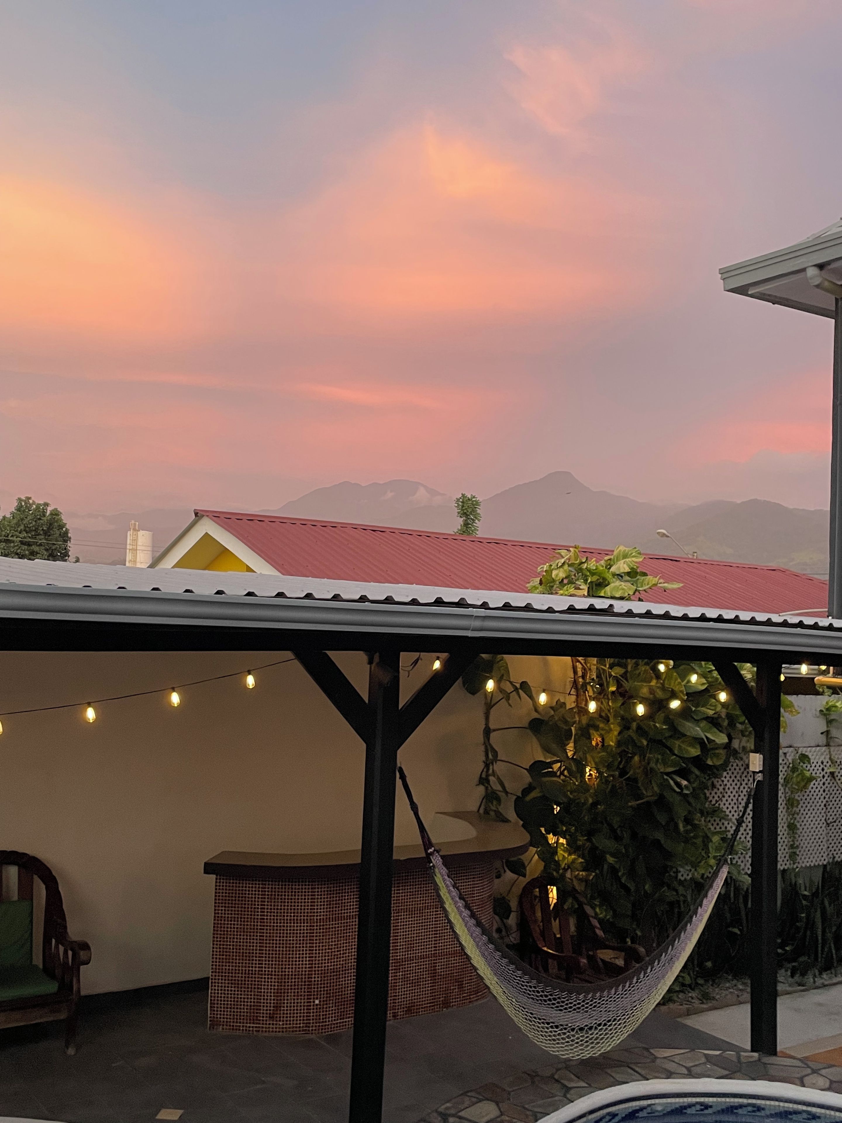 A covered outdoor area with a hammock, string lights, and a view of distant mountains.