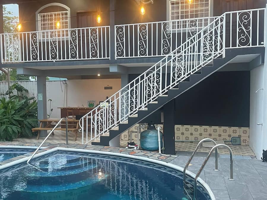 Une piscine dotée d’une balustrade blanche et d’un escalier menant à une terrasse supérieure, agrémentée d’un éclairage extérieur.