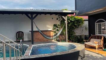 A swimming pool with a hot tub, a hammock, and outdoor furniture.