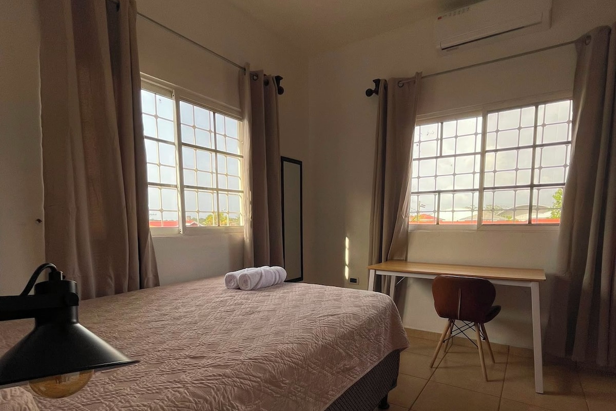 A bedroom with a bed, a desk, and two windows.