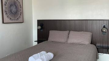 A hotel room with a large bed, two pillows, a headboard with vertical lines, a wall-mounted light fixture, and a framed abstract artwork.