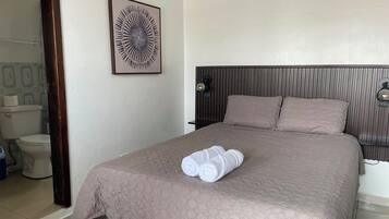 Una camera d'albergo con un letto, una testiera, una lampada a parete e un quadro incorniciato.