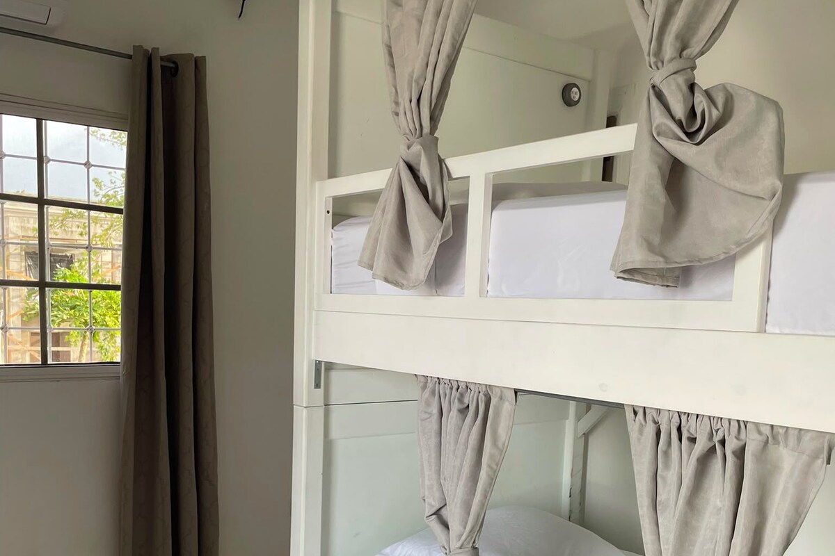 A bunk bed with curtains tied at the headboard, a window with curtains, and a tiled floor.