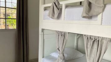 Een stapelbed met gordijnen vastgemaakt bij het hoofdeinde, een raam met gordijnen en een betegelde vloer.