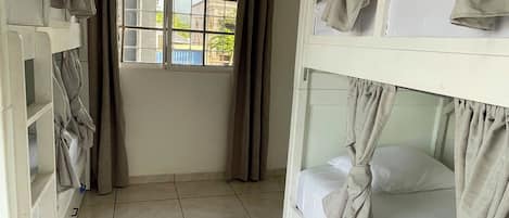 A room with bunk beds, a window with curtains, and a tiled floor.
