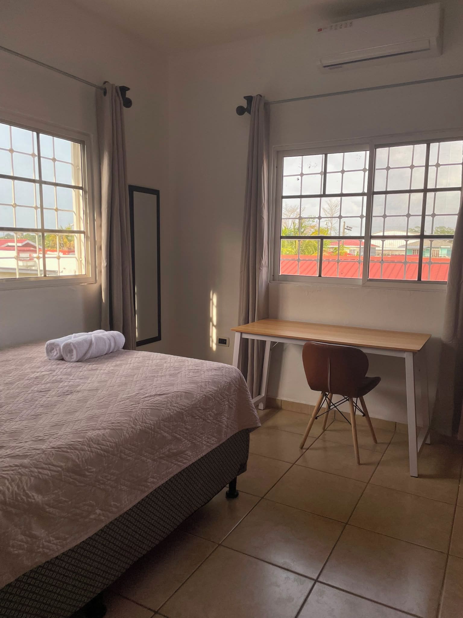 A hotel room with a bed, a desk, and a view of a red-roofed building.