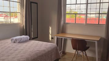 A hotel room with a bed, a desk, and a view of a red-roofed building.