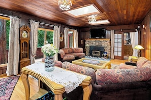 A cozy living room with a fireplace, patterned sofas, a wooden coffee table, and a large clock.