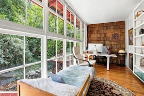 A room with a large window, a bed, a desk with a computer, and a wooden wall.