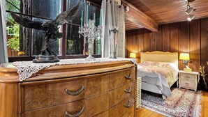 A wooden bedroom with a bed, nightstand, dresser, and a window with curtains.