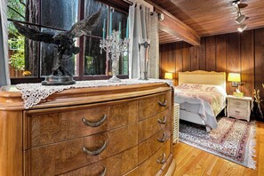 Un dormitorio de madera con cama, mesita de noche, cómoda y ventana con cortinas.