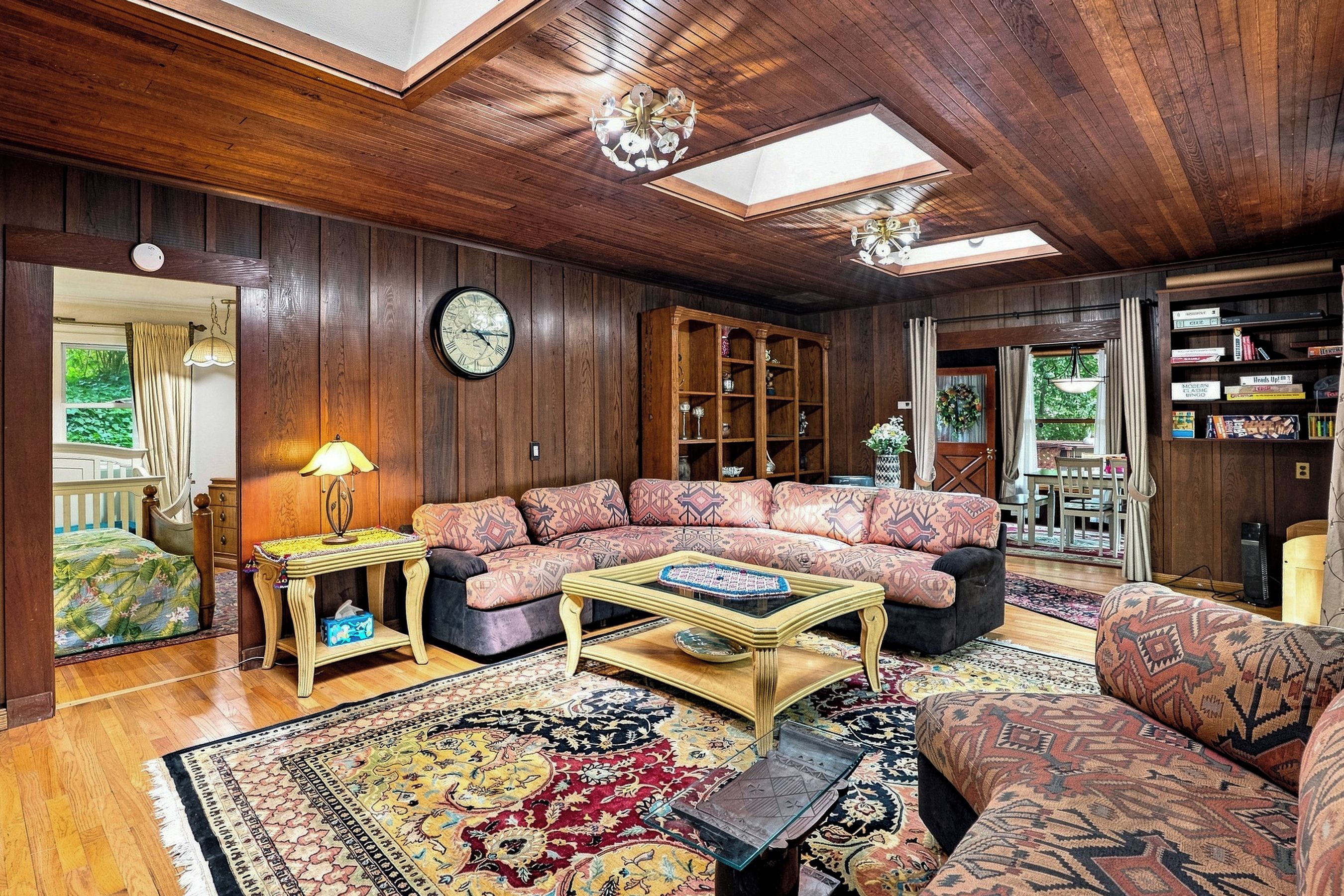 A cozy living room with a wooden ceiling, a large sofa, a coffee table, and a patterned rug.
