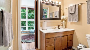 A bathroom with a vanity, a mirror with lights, a toilet, and a window with a view of greenery.