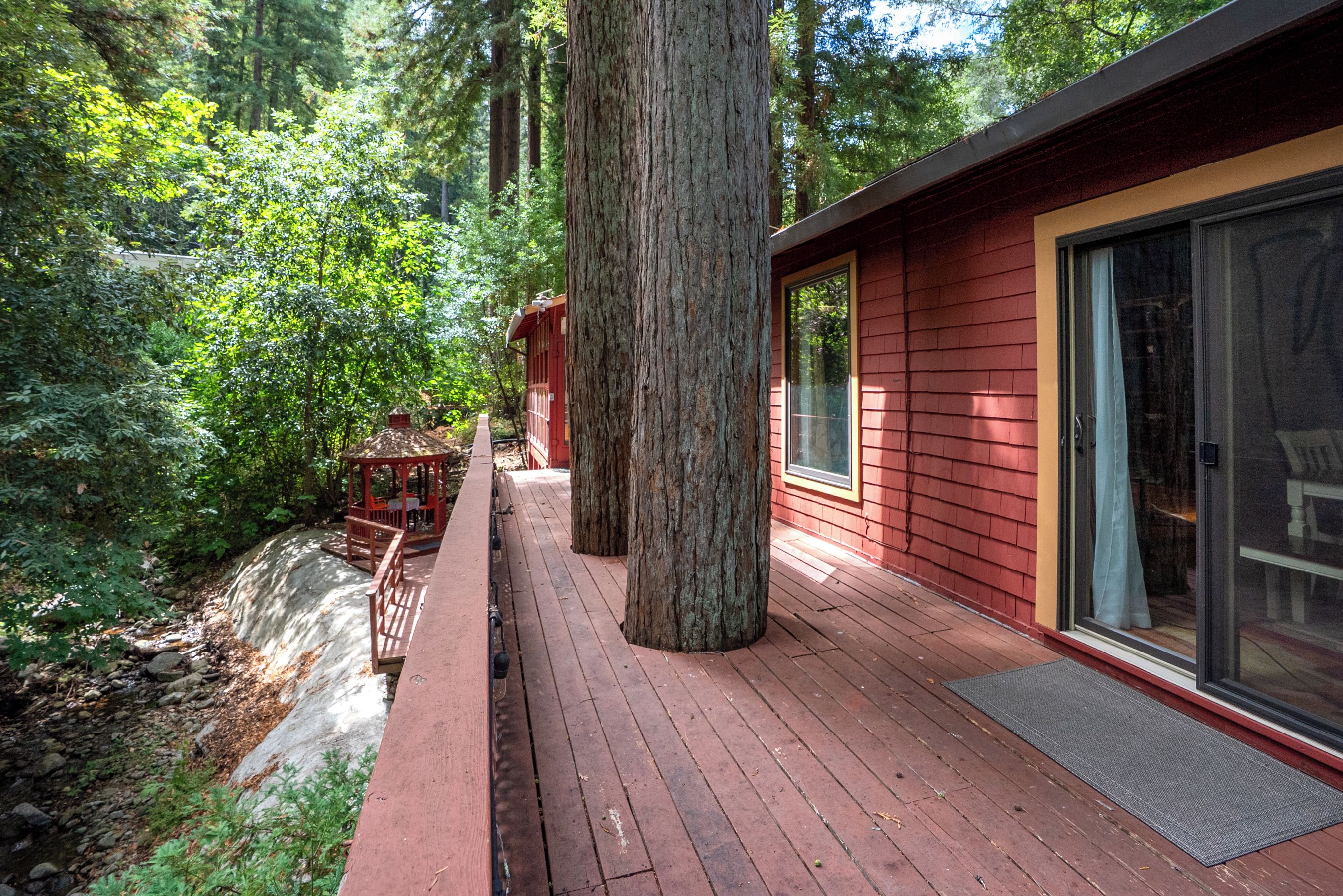 A wooden deck with a glass door leading to a red building, surrounded by a forest.