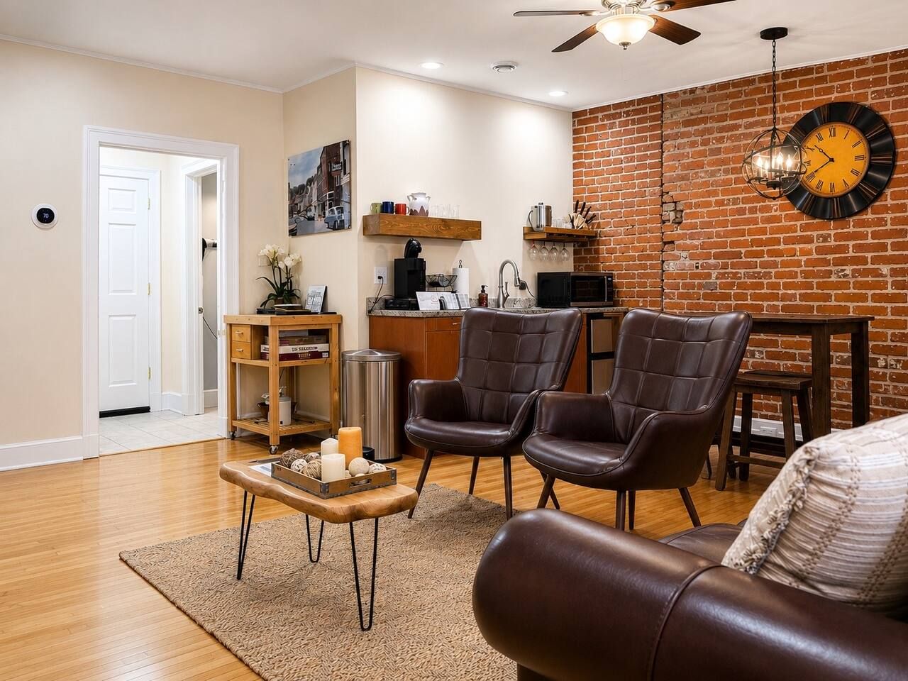 A living room with a brown leather sofa, two leather chairs, a coffee table, and a brick wall with a clock.