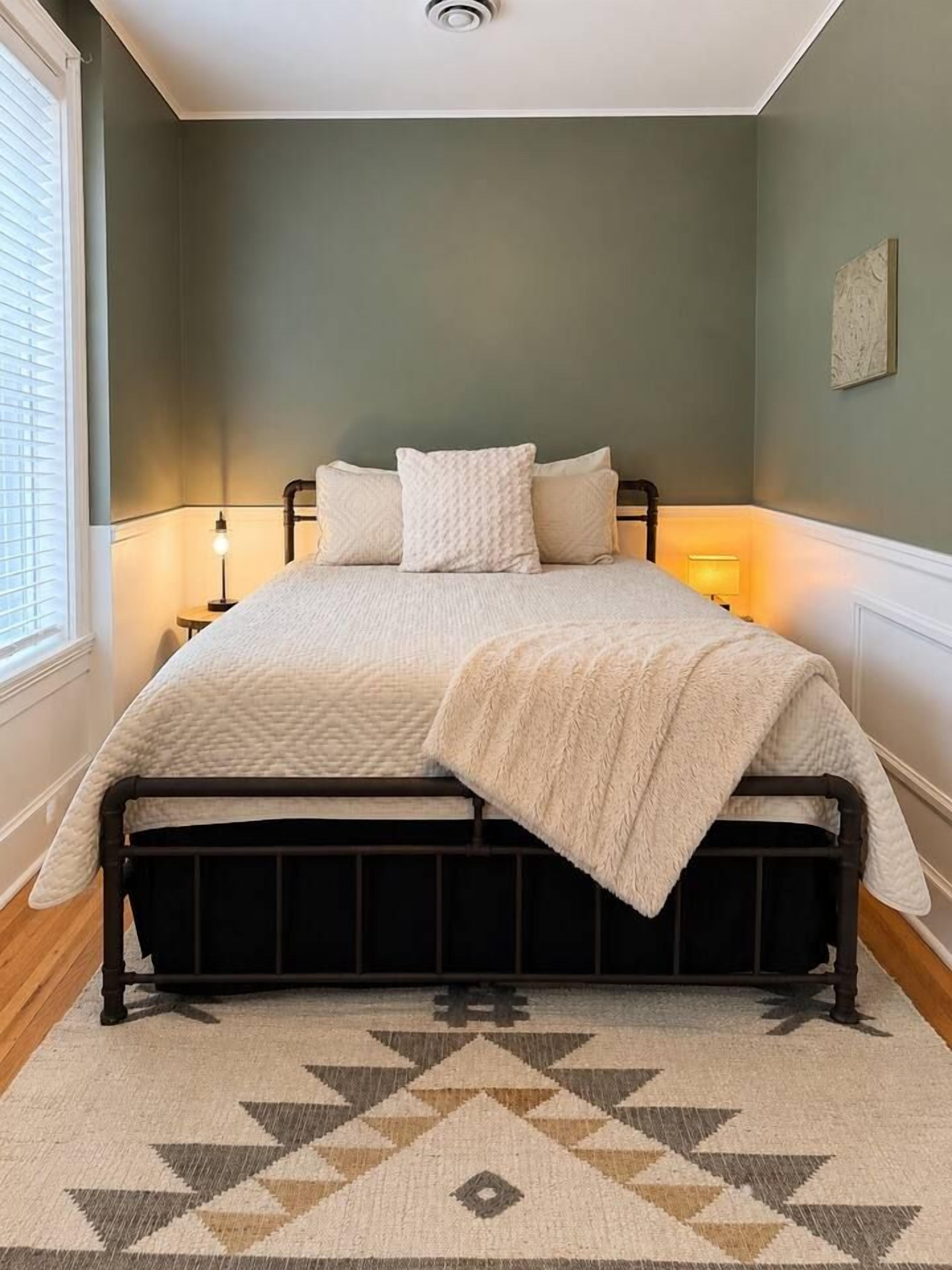 A bedroom with a bed, bedside lamps, and a patterned rug.