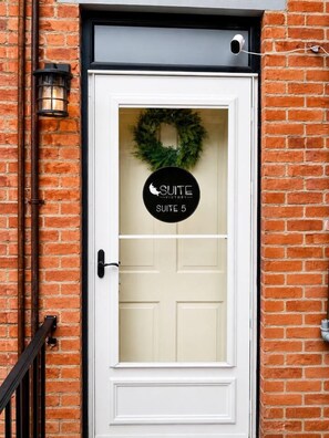 A white door with a frosted glass panel, a black sign reading 'SUITE 5', and a wreath above the door. - Suite Victory #5 On Main St w/Reserved Parking (Galena)