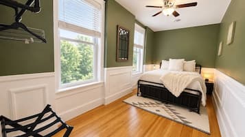 Un dormitorio con cama, ventilador de techo, ventana y una silla.