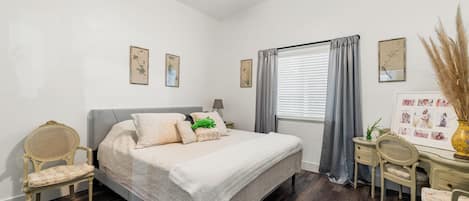 Un dormitorio con cama, dos sillones, un escritorio y una ventana con cortinas.