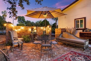 An outdoor patio with a brick floor, a round table with chairs, a sofa, a large umbrella, and string lights. - Newly Constructed 1-bedroom guest house near Arden Park (Sacramento)