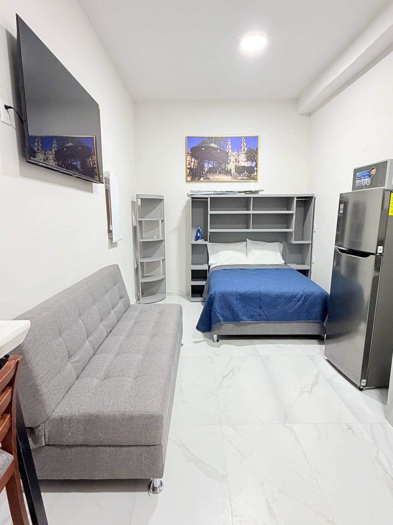 Un dormitorio con cama, sofá, televisión y refrigerador.