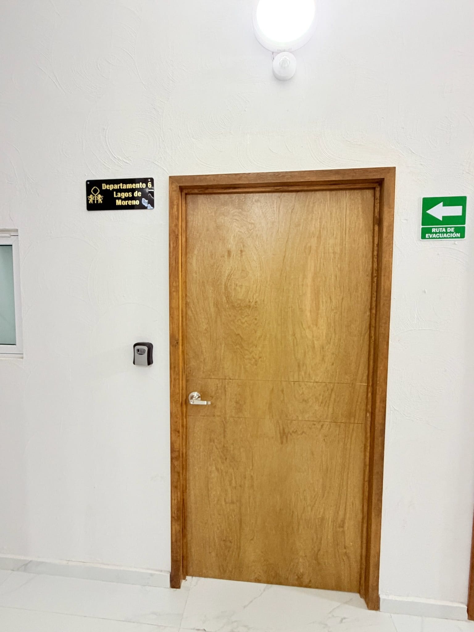 A wooden door with a keyhole and a door handle, a sign indicating 'Departamento 6 Lagoes de Moreno', and a green evacuation route sign.