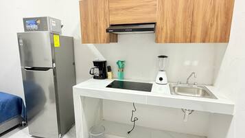 Una kitchenette funcional con refrigerador, estufa, pileta y gabinetes de madera.