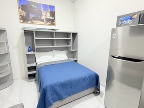 Habitación de hotel compacta con cama, armario empotrado, una pequeña zona de estar y refrigerador.