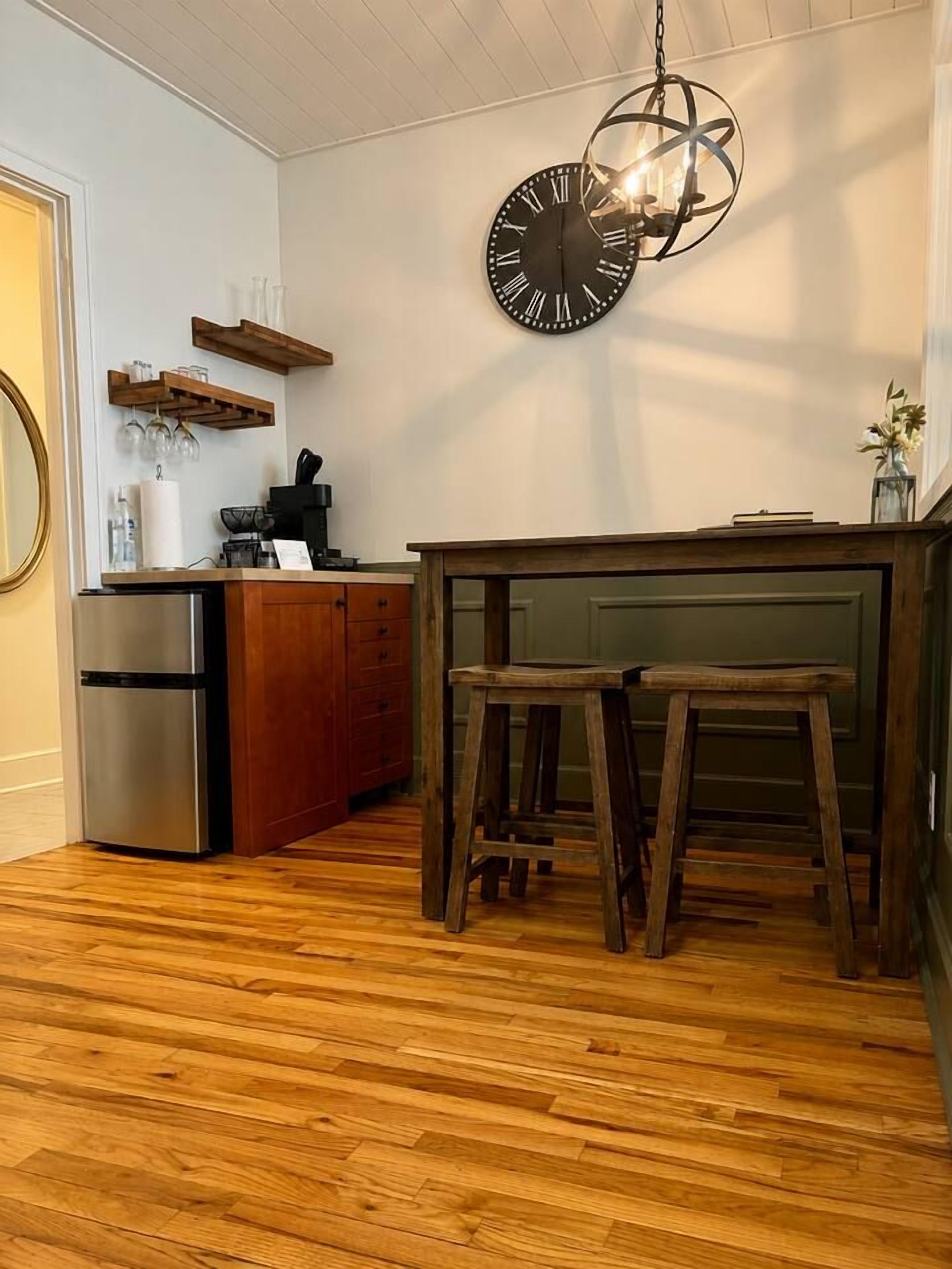 Eine Küche mit Holzboden, einem Holztisch mit Hockern, einer Pendelleuchte und einer Wanduhr.