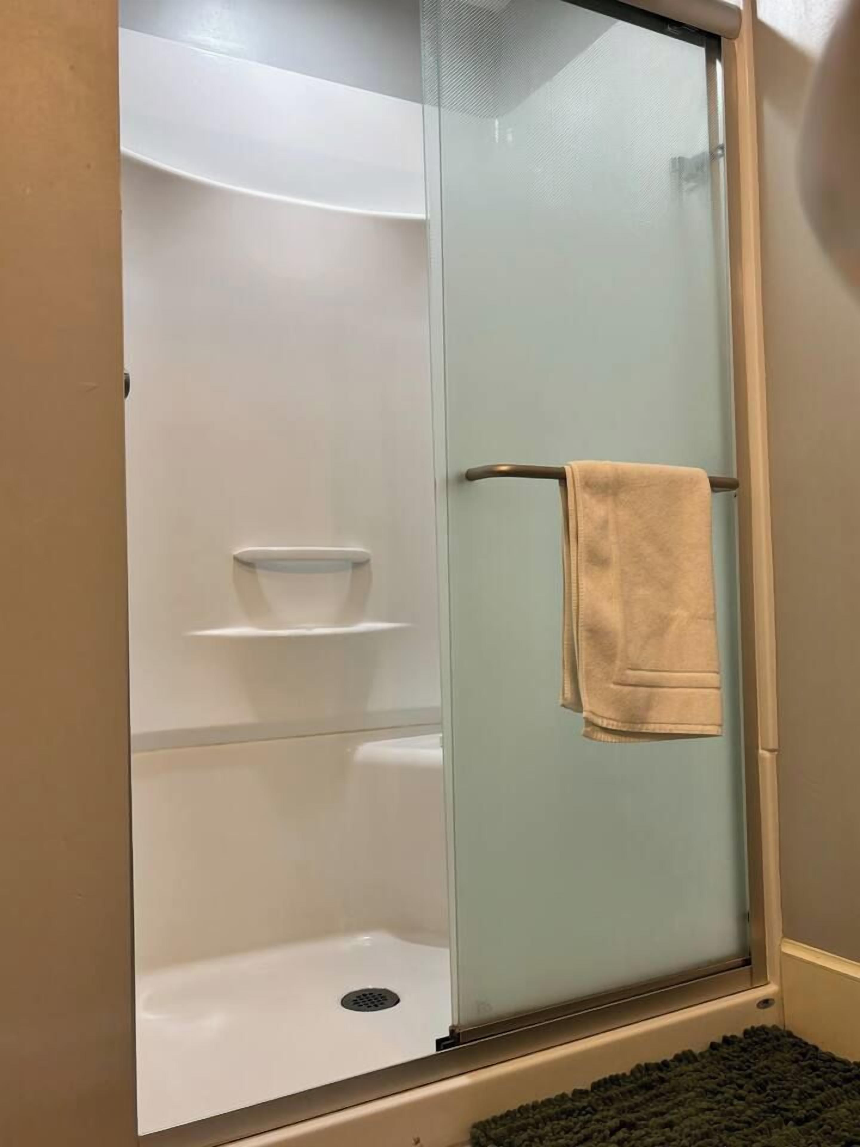 Een douche met glazen wand, een handdoekrek en een plank.