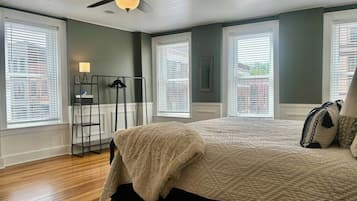 Un dormitorio con una cama, una lámpara de pie, un ventilador de techo y ventanas amplias.