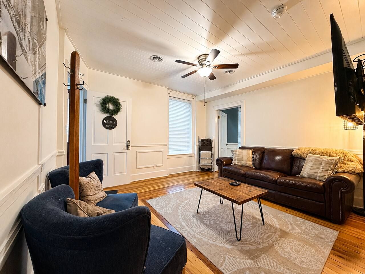 A living room with a ceiling fan, a brown leather sofa, a blue armchair, and a wooden coffee table.