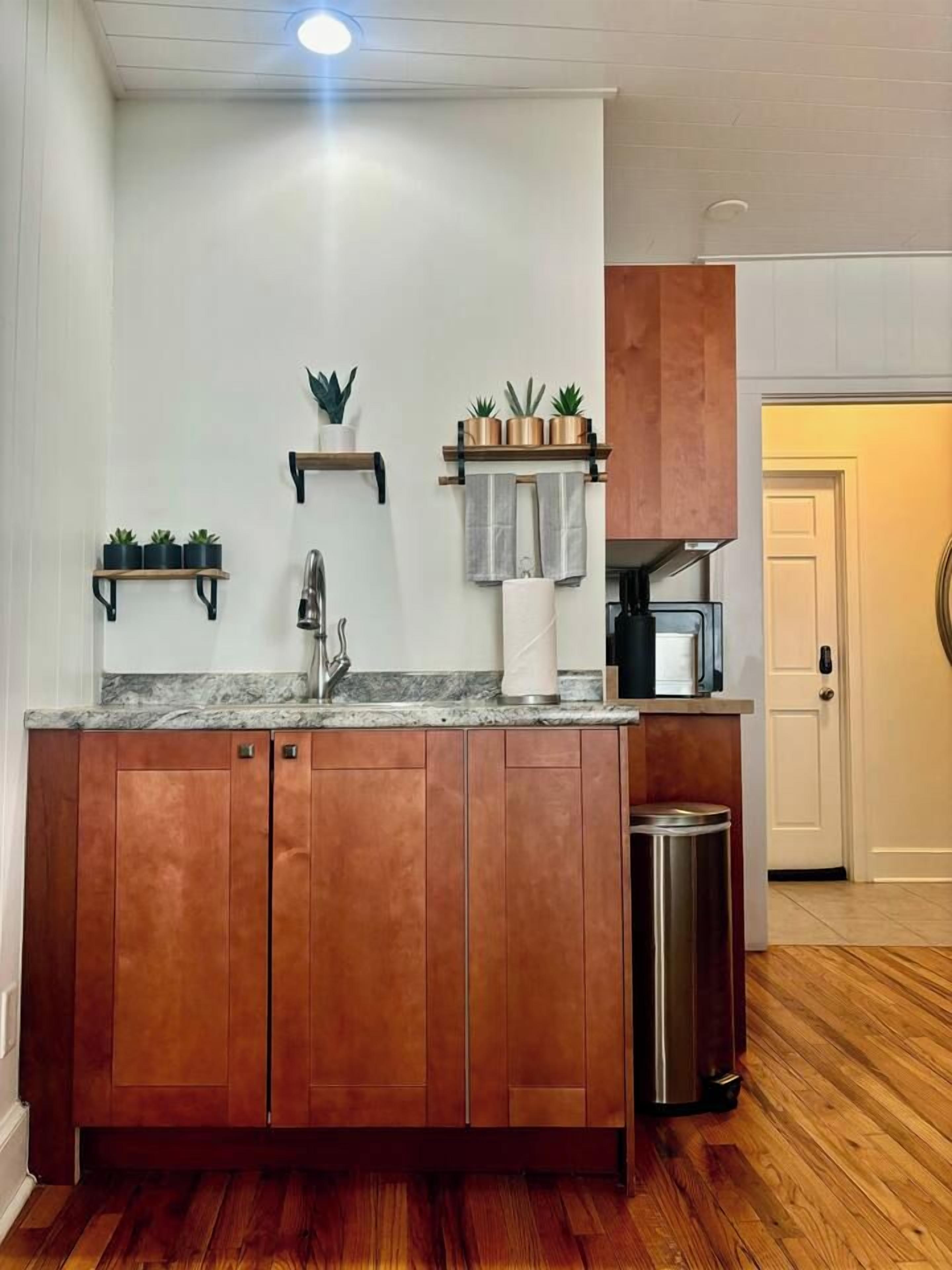 A kitchen with wooden cabinets, a stainless steel sink, a countertop, and a trash can.