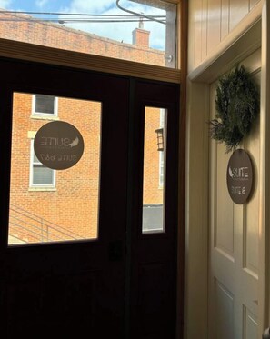 A hotel entrance with a sign indicating 'Suite 6' and a window view of a brick building.