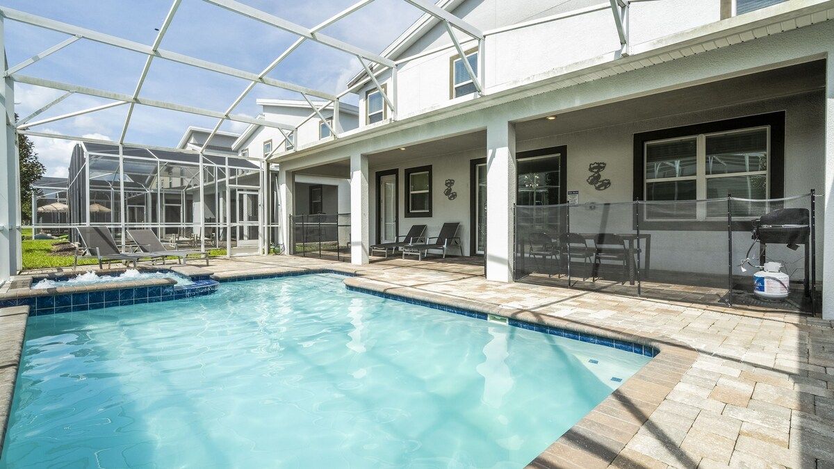 A swimming pool with a glass enclosure, lounge chairs, and a barbecue area.