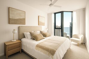 Ein Hotelzimmer mit einem großen Bett, einem Nachttisch, einem Sessel und Blick auf den Ozean.