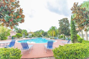 A pool area with blue chairs and a clear blue pool. - Elegant 3BR Home | Gated Community | Shared Amenities & Pool (Kissimmee)