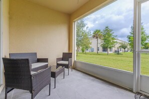 A room with two wicker chairs and a small table, a large window with a view of a grassy area and buildings. - Elegant 3BR Home | Gated Community | Shared Amenities & Pool (Kissimmee)