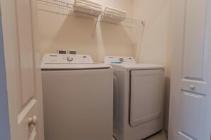 A laundry area with two white front-loading washing machines and a metal drying rack above them. - Elegant 3BR Home | Gated Community | Shared Amenities & Pool (Kissimmee)