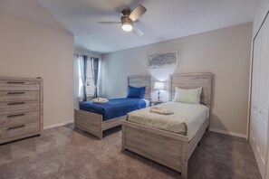 A bedroom with two beds, a ceiling fan, a nightstand, a lamp, and a painting on the wall. - Elegant 3BR Home | Gated Community | Shared Amenities & Pool (Kissimmee)