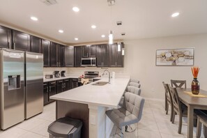 A modern kitchen with stainless steel appliances, dark cabinetry, and a central island with bar seating. - Elegant 3BR Home | Gated Community | Shared Amenities & Pool (Kissimmee)
